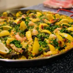 Paella z owocami morza, cytryną i groszkiem w dużej patelni.
